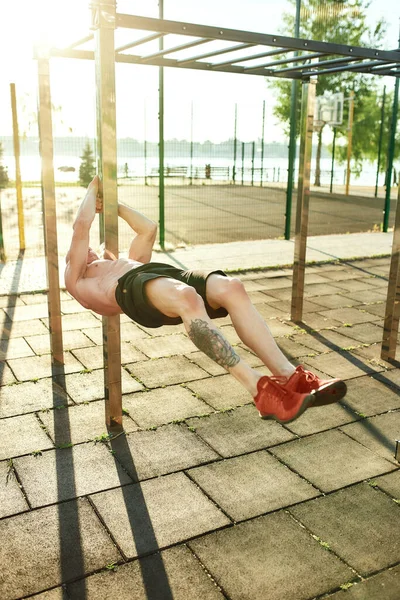 Atleta caucásico muscular colgando horizontalmente en terreno deportivo —  Fotos de Stock