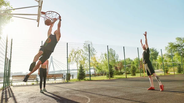 Filmagem completa de jovens ativos passando tempo ao ar livre no playground. Habilidade desportiva cara jogando bola na cesta, enquanto joga basquete — Fotografia de Stock