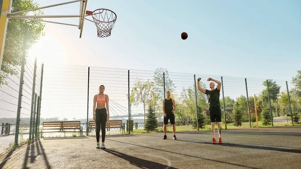 Tiga teman olahraga menghabiskan waktu bersama di luar ruangan di taman bermain, bermain basket di hari yang cerah — Stok Foto