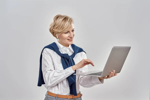 Ritratto di elegante donna caucasica di mezza età che indossa abiti da lavoro con laptop in mano, mentre ha una videochiamata online, isolata su sfondo grigio — Foto Stock