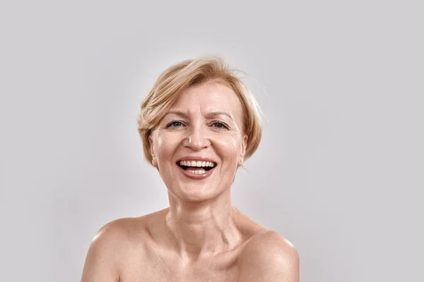 Primer plano retrato de una atractiva mujer de mediana edad sonriendo a la cámara mientras posaba, de pie sobre un fondo gris. Expresiones faciales humanas, emociones, concepto de reacción —  Fotos de Stock