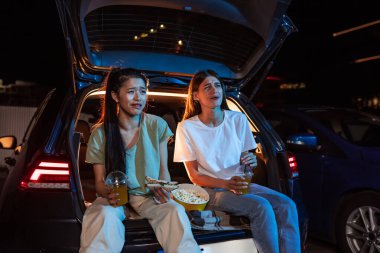 İki genç kadın, en iyi arkadaşlar araba bagajında otururken, abur cubur yerken ve akşamları açık hava sinemasında film izlerken duygusal görünüyorlar.