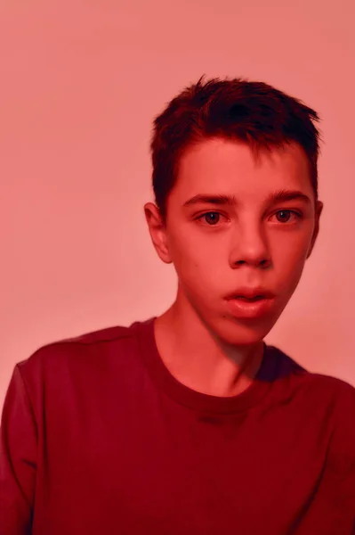 Close up portrait of teenaged disabled boy with cerebral palsy looking away, posing isolated over red light background — Stock Photo, Image