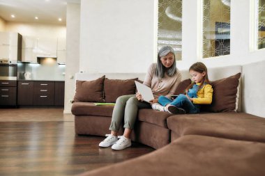 Küçük kız büyükannenin yanında otururken tabletle oynuyor.