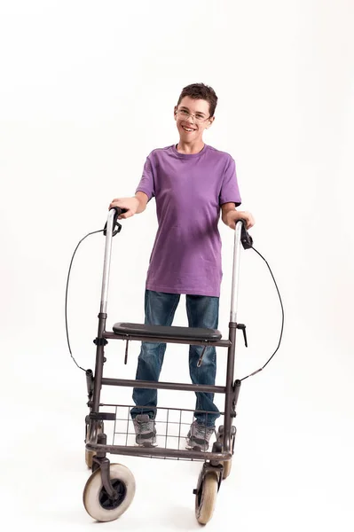 Full length shot of teenaged disabled boy with cerebral palsy in the glasses smiling at camera, taking steps with his walker isolated over white background — Stock Photo, Image