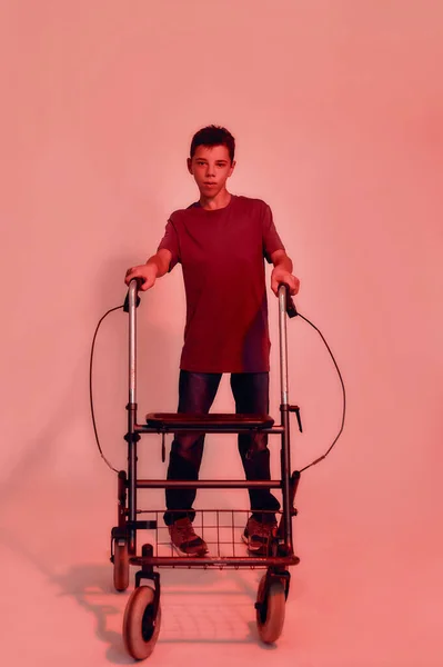 Largometraje completo del adolescente discapacitado con parálisis cerebral mirando a la cámara, dando pasos con su caminante aislado sobre fondo de luz roja — Foto de Stock