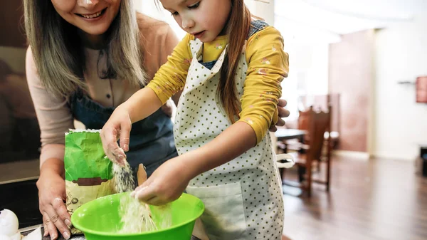 Kleines Mädchen gießt neben Großmutter Mehl in große Schüssel — Stockfoto