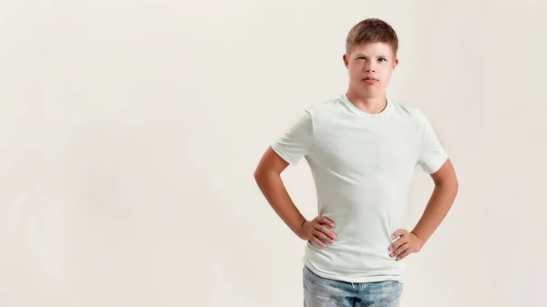 Remaja cacat anak laki-laki dengan sindrom Down melihat kamera sambil berpose, berdiri dengan tangan di atas pinggang terisolasi di atas latar belakang putih — Stok Foto