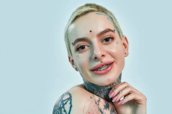 Retrato de una mujer blanca con piercing y tatuajes mirando a una cámara con la mano cerca de la cabeza — Foto de Stock