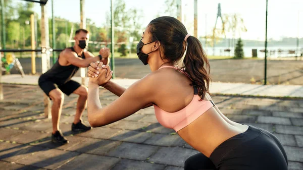 Maskeli genç kadın sporcunun yanında çömeliyor.