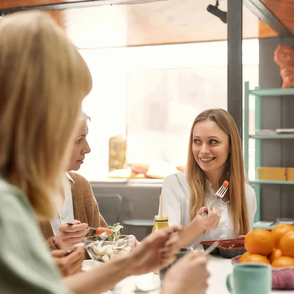 Una mujer de pelo rubio de mediana edad bien vestida sonriendo y sentada en una mesa con sus colaboradoras comiendo — Foto de Stock