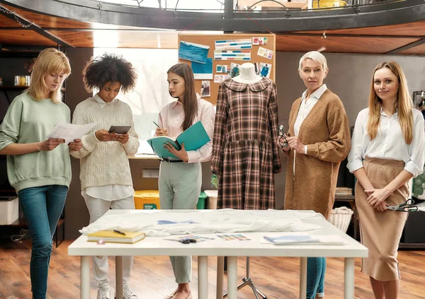 Öt divatosan öltözött, különböző korú nő, és együtt versenyeznek az asztal körül egy reggeli ötletbörze alatt, miközben a kamerába néznek. — Stock Fotó