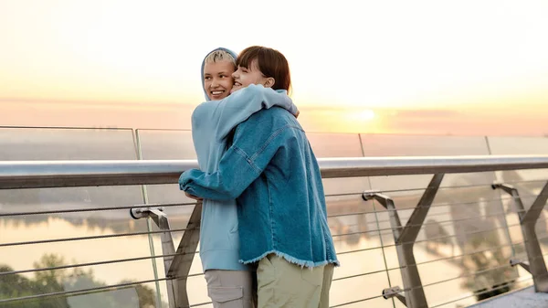Young loving lesbian couple cuddling and looking happy, Two women enjoying romantic moments, standing on the bridge together at sunrise — Stock Photo, Image