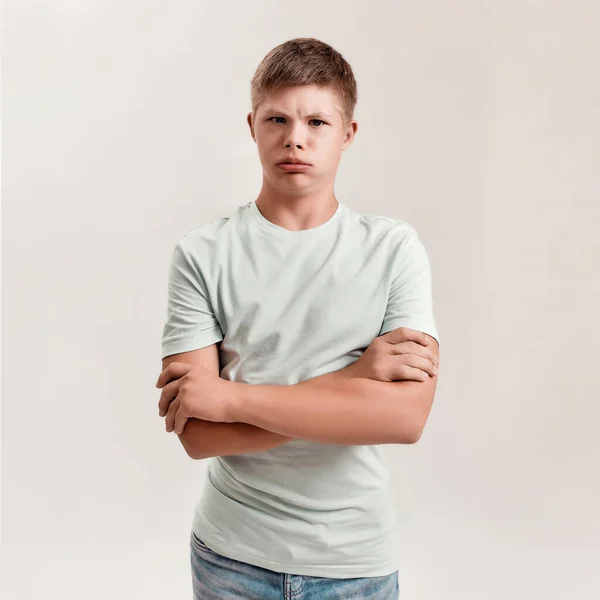 Portrait of teenaged disabled boy with Down syndrome making funny faces, looking grumpy at camera while posing isolated over white background — Stock Photo, Image