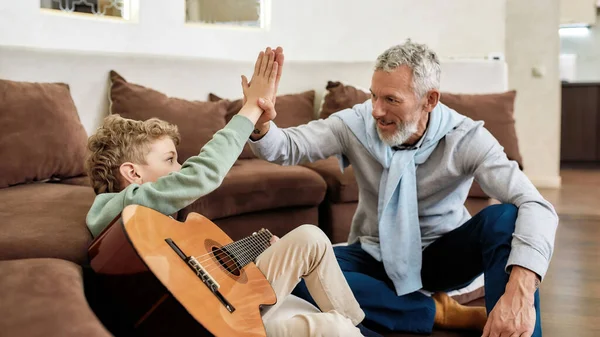 Büyükbaba ve torun oturup gitar çalmayı öğrettikten sonra beşlik çakıyor. — Stok fotoğraf