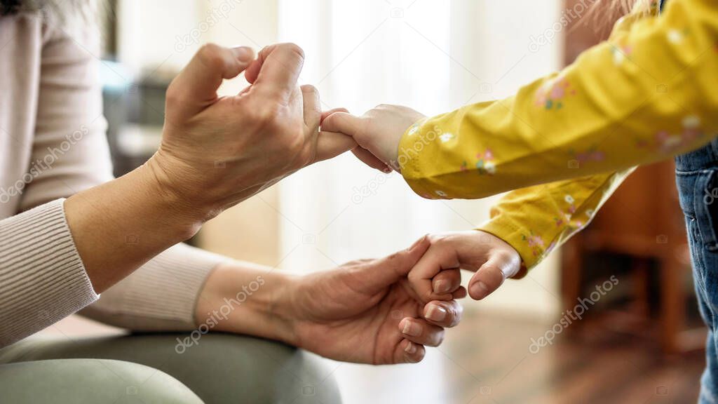 Pinky swear. Close up of mature grandmother and little granddaughter holding pinkie fingers while spending time together at home