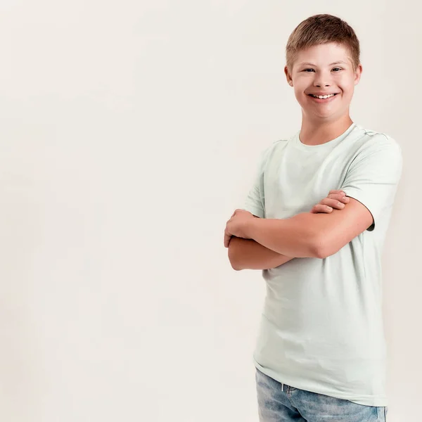 Anak cacat gembira dengan sindrom Down tersenyum ke kamera sambil berpose, berdiri dengan lengan terisolasi di atas latar belakang putih — Stok Foto
