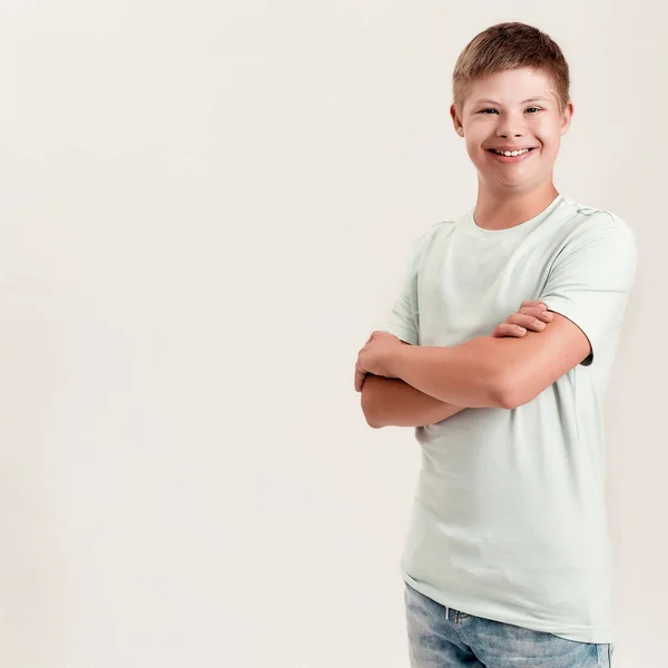 Joyful gehandicapte jongen met Down syndroom glimlachen op de camera terwijl poseren, staan met armen gekruist geïsoleerd over witte achtergrond — Stockfoto