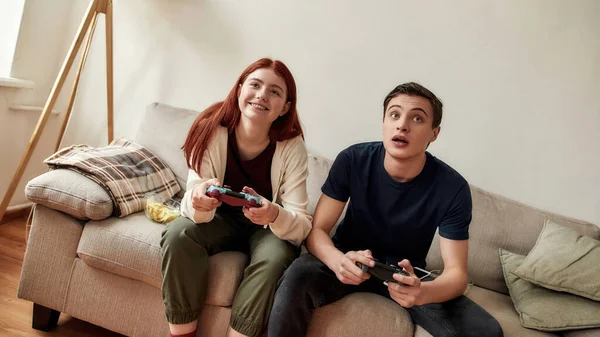 Young couple looking focused, holding game console while playing video games together, sitting on the couch in the living room