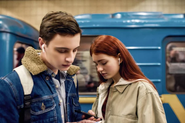 Portrét páru teenagerů zcela pohlcen používáním chytrých telefonů, ignorovat jeden druhého, zatímco stojí spolu na stanici metra — Stock fotografie