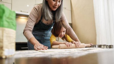 Küçük kız yemek pişirirken büyükannesiyle hamur topluyor.