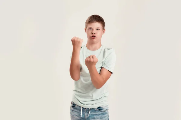 Alegre niño discapacitado con síndrome de Down mirando a la cámara, de pie con los puños apretados, sintiéndose fuerte aislado sobre fondo blanco —  Fotos de Stock