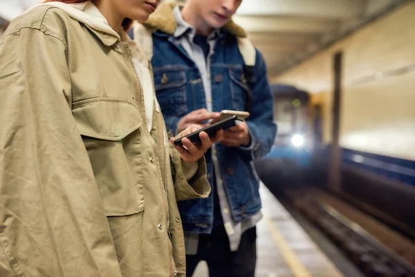 Περικοπή πλάνο των νέων που χρησιμοποιούν smartphones, ενώ περιμένουν για το τρένο στο σταθμό του μετρό. Μερικοί έφηβοι που χρησιμοποιούν την εφαρμογή για κινητά, ελέγχουν το πρόγραμμα δημόσιων συγκοινωνιών — Φωτογραφία Αρχείου