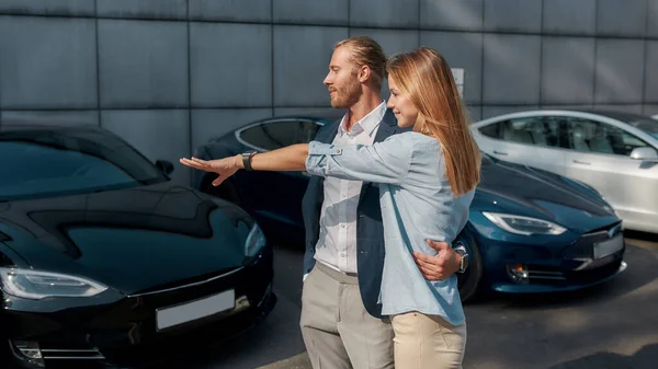 Gelukkige jonge vrouw wijzend naar auto in showroom — Stockfoto