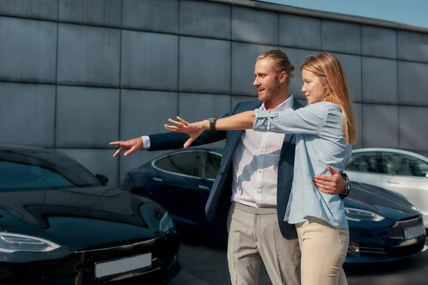 Galeride kucaklaşırken arabayı gösteren genç bir çift.