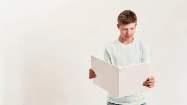 Garçon handicapé adolescent avec trisomie 21 regardant concentré tout en lisant un livre, debout isolé sur fond blanc — Photo