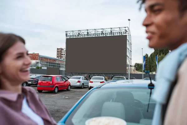Молодая девушка смеется с мужчиной возле машины во время сеанса кино — стоковое фото