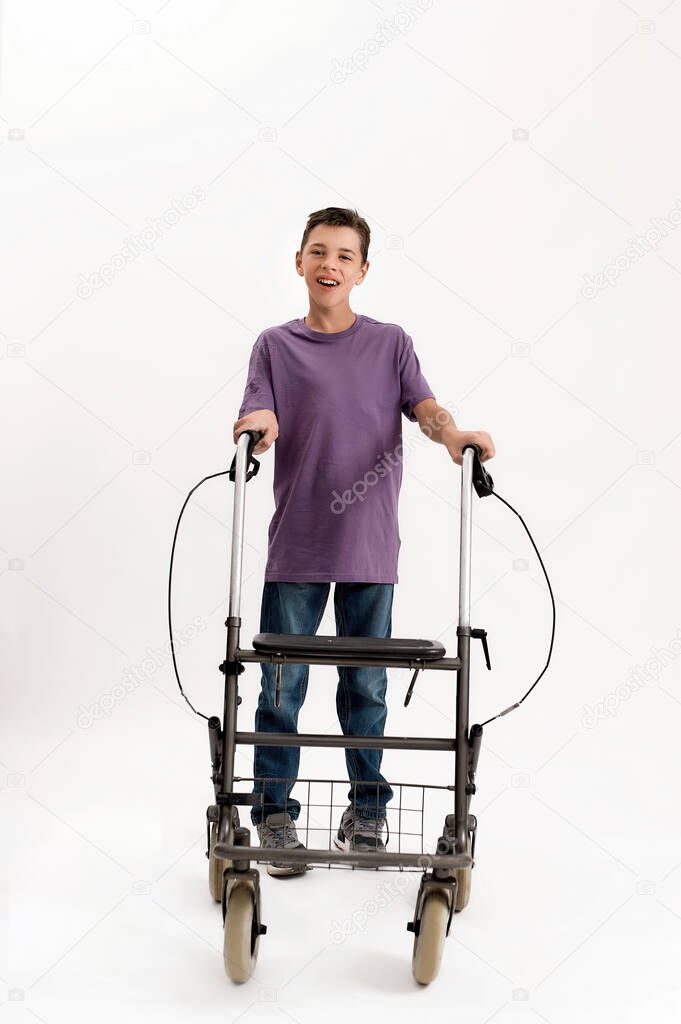 Full length shot of happy teenaged disabled boy with cerebral palsy looking at camera, taking steps with his walker, standing isolated over white background