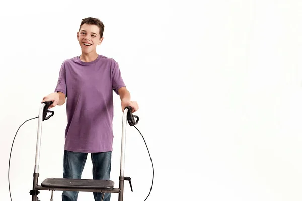 Щасливий хлопчик-підліток з інвалідністю з церебральним паралічем посміхається на камеру, робить кроки, використовуючи його ходунки ізольовані на білому тлі — стокове фото