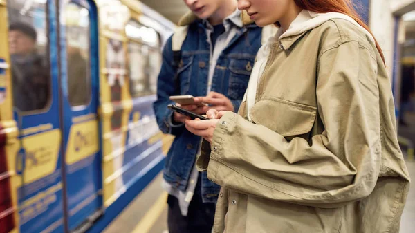 Καλλιεργημένη φωτογραφία νέων που χρησιμοποιούν smartphones στο σταθμό του μετρό. Μερικοί έφηβοι που χρησιμοποιούν την εφαρμογή για κινητά, ελέγχουν το πρόγραμμα δημόσιων συγκοινωνιών — Φωτογραφία Αρχείου