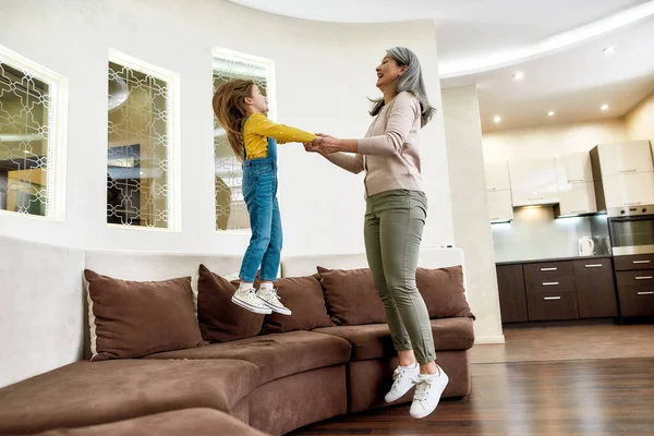 Leuke tijd. gelukkig kleindochter springen op een bank terwijl het hebben van plezier met haar vrolijke oma thuis — Stockfoto