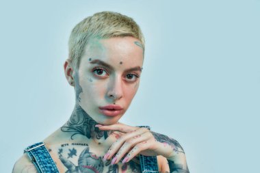 Dövme ve piercing. Yüzüne piercing takmış, başı hafifçe eğilmiş ve kameraya bakan beyaz dövmeli bir kadın.