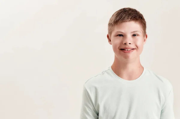 Retrato de menino desativado alegre com síndrome de Down sorrindo para a câmera enquanto posando isolado sobre fundo branco — Fotografia de Stock