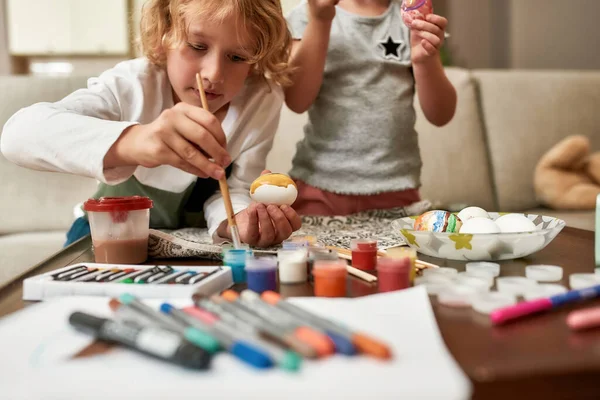 Zblízka roztomilý malý chlapec malování barevné velikonoční vajíčka spolu s jeho sourozeneckou sestru, zatímco tráví čas doma — Stock fotografie