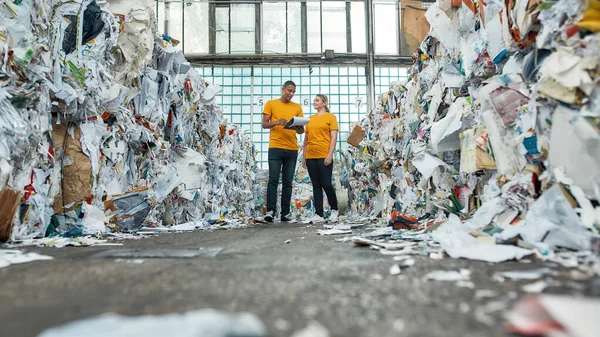 Man with woman standing between piles of waste paper