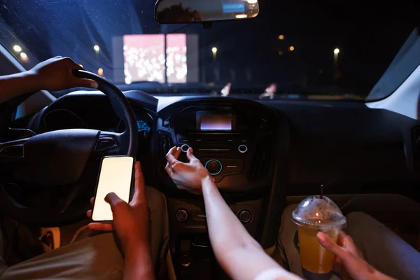 Κοντινό πλάνο της γυναίκας που αγγίζει το κουμπί στο ταμπλό του αυτοκινήτου, ενώ ο οδηγός κρατώντας ένα smartphone με κενή οθόνη στο χέρι του — Φωτογραφία Αρχείου