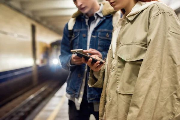Περικοπή πλάνο των νέων που χρησιμοποιούν smartphones, ενώ περιμένουν για το τρένο στο σταθμό του μετρό. Μερικοί έφηβοι που χρησιμοποιούν την εφαρμογή για κινητά, ελέγχουν το πρόγραμμα δημόσιων συγκοινωνιών — Φωτογραφία Αρχείου