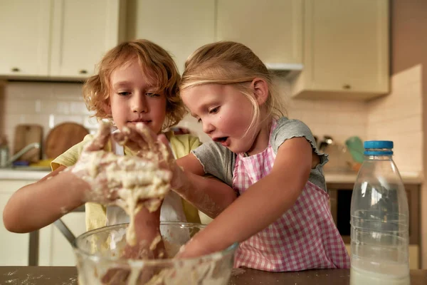 Arkadaşız. Sevimli küçük çocuklar, önlüklü kız ve erkek masada hamuru hazırlarken heyecanlı görünüyorlar. Çocuklar mutfakta kurabiye yaparken eğleniyor. — Stok fotoğraf