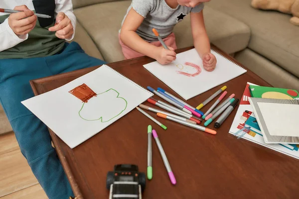 Keçeli kalemle kağıda resim çizen küçük çocuklar, evdeki kanepede yan yana oturuyorlar. — Stok fotoğraf