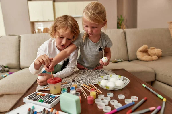 Kreativita. Roztomilé malé děti, chlapec a dívka malování barevné velikonoční vajíčka v obývacím pokoji, zatímco tráví čas spolu doma — Stock fotografie