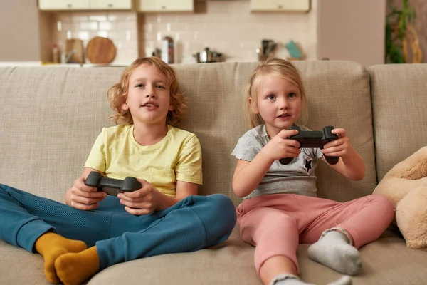 Freizeit. Fröhliche Kinder, kleine Jungen und Mädchen, die Videospiele mit Steuerknüppel oder Controller spielen, während sie zu Hause zusammen auf dem Sofa sitzen — Stockfoto