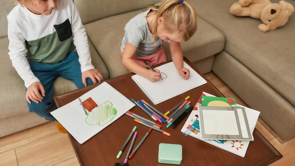 Beskuren bild av små barn, pojke och flicka ritning på papper med markeringspenna, sitter tillsammans på en soffa hemma — Stockfoto