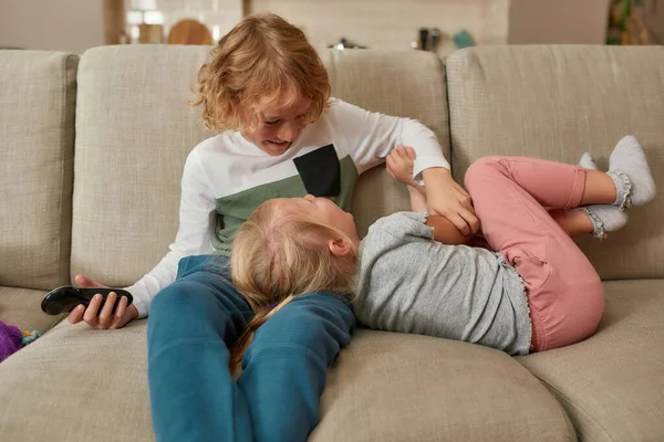 Beaux petits frères et sœurs, garçon et fille qui s'amusent, jouant ensemble en regardant la télévision, se blottissant sur un canapé à la maison — Photo