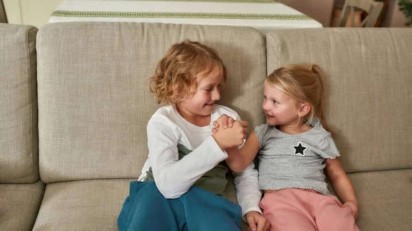 Porträtt av glada små barn, pojke och flicka ler mot varandra, leker, har armbrytning tävling tillsammans på en soffa hemma — Stockfoto
