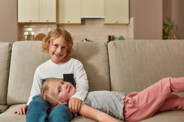 Retrato de niños pequeños y lindos, niño y niña sonriendo a la cámara mientras pasan tiempo juntos, abrazándose en un sofá en casa —  Fotos de Stock