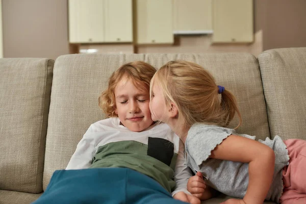 Un doux baiser. Portrait de mignonne petite fille embrasser son frère frère frère tout en passant du temps ensemble, câlins sur un canapé à la maison — Photo